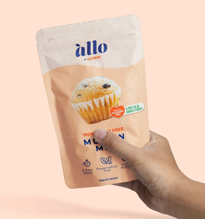 An Allo muffin mix pouch held in a hand against a soft pink background.